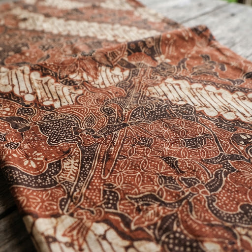 Tekstur kain batik tradisional berwarna cokelat tanah dengan motif klasik yang rumit